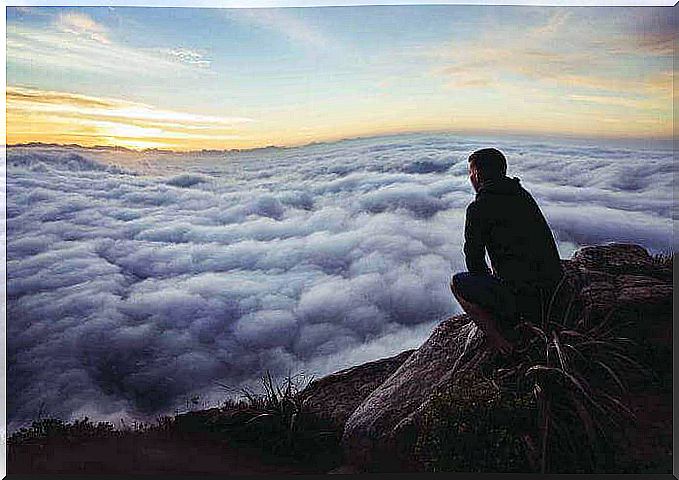 Man bent over mountain looking at clouds