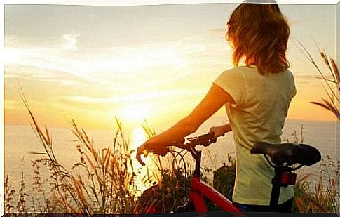 Woman with bicycle while watching sunrise and feeling motivated